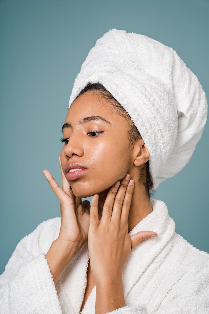 Calm African American female in bathrobe touching face against blue background